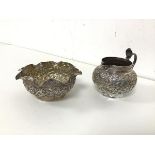 An Indian white metal milk jug and sugar bowl, both with foliate decoration to body, sugar bowl with