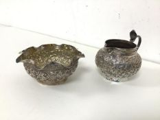 An Indian white metal milk jug and sugar bowl, both with foliate decoration to body, sugar bowl with