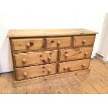 A pine chest of drawers with an arrangement of seven drawers, on plinth base (73cm x 127cm x 43cm)