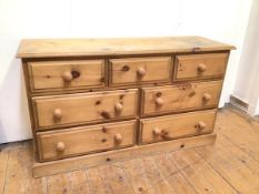 A pine chest of drawers with an arrangement of seven drawers, on plinth base (73cm x 127cm x 43cm)