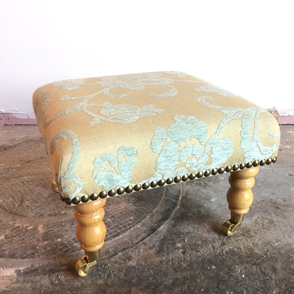 A modern square footstool in floral upholstery, on turned supports ending in castors (32cm x 47cm
