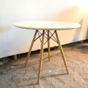 A white circular top dining table on four splay tapering beech supports united by vertical X