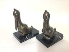 A pair of French Art Deco patinated metal bookends, Franjou, modelled as pelicans, each with glass