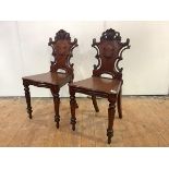 A pair of Victorian mahogany hall chairs, each back carved with scrolls and central vacant