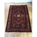 A Shiraz hand-knotted wool small carpet, the madder field with indigo framed medallion and