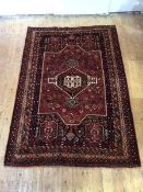 A Shiraz hand-knotted wool small carpet, the madder field with indigo framed medallion and