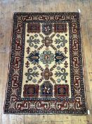 A hand-knotted wool rug of Kazak design, the dark cream field decorated with stylised flowerheads