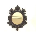 An early 20th century Black Forest carved wall mirror, the oval plate within an urn-surmounted