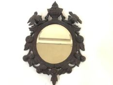 An early 20th century Black Forest carved wall mirror, the oval plate within an urn-surmounted