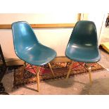 A pair of moulded plastic teal chairs on splay beech supports united by vertical X stretchers (