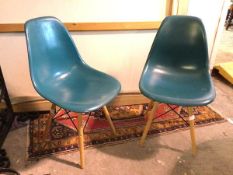 A pair of moulded plastic teal chairs on splay beech supports united by vertical X stretchers (