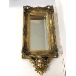 A modern composition wall mirror, the bevelled glass within a gilt pierced elaborate frame above a