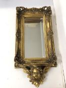 A modern composition wall mirror, the bevelled glass within a gilt pierced elaborate frame above a