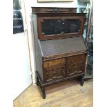 A 1920s/30s Tudor style oak bureau bookcase, with glazed fold up door above a tambour front, lacking