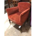 An Edwardian armchair in a brick red upholstery, on turned front supports terminating in four