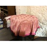 A modern circular footstool, the buttoned top with a pink and sand coloured cover, attached to