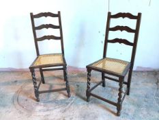 A pair of 1920s/30s oak side chairs with moulded ladder back above caned seats, with barley twist