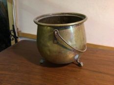 A brass and copper cauldron, lacking lid, with swing handle on three ball and claw feet (28cm x