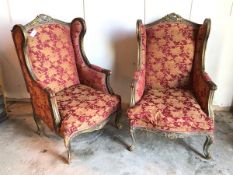 A pair of Louis XV style wing back armchairs with foliate upholstery in brick reds and yellows, on