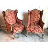 A pair of Louis XV style wing back armchairs with foliate upholstery in brick reds and yellows, on