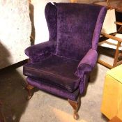 A wing back armchair with scroll arms in purple upholstery on front cabriole legs ending in pad feet