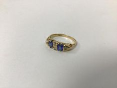 An 18ct gold ring set two blue stones separated by a pair of diamonds and flanked by single diamonds