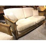 An Ercol three seater sofa with caned sides and cushions in sand corduroy upholstery, stamped