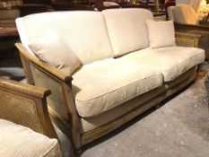 An Ercol three seater sofa with caned sides and cushions in sand corduroy upholstery, stamped