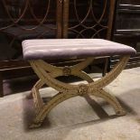 A white painted curule footstool with upholstered top on foliate decorated supports united by
