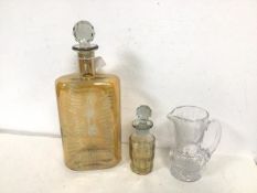 A large cut glass decanter with light yellow colouring and stopper (34cm), a small decanter with