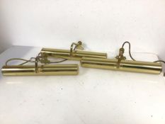 A set of three brass picture lights, each with cylindrical shade, suspended from curved arm (each: