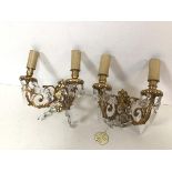 A pair of gilt metal wall lights, each with a pair of faux candles over a drip tray, on C scroll
