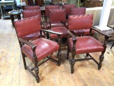 A set of eight Tudor style oak armchairs with brick red upholstered backs and seats in leathercloth,