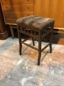 A 1920s stool with distressed upholstered seat above a galleried apron, the supports united by