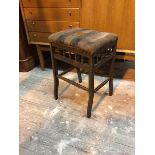 A 1920s stool with distressed upholstered seat above a galleried apron, the supports united by