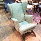 A 1950s/60s sprung Wing back rocking chair with scroll arms in a mottled green upholstery (80cm x