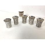 A set of five Indian white metal cups, each with a flared rim and foliate engraved body (6cm x