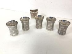 A set of five Indian white metal cups, each with a flared rim and foliate engraved body (6cm x