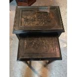 A pair of ebonised Chinese nesting tables, each with a deep relief carved top depicting Soldiers