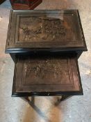 A pair of ebonised Chinese nesting tables, each with a deep relief carved top depicting Soldiers