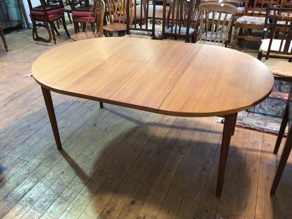 A mid century style circular teak extending dining table, with two leaves stored below top, on