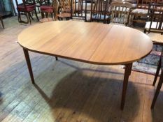 A mid century style circular teak extending dining table, with two leaves stored below top, on