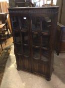 An oak bookcase, with two doors each of six glass panels above two linenfold panels, the interior