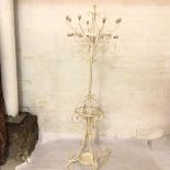 A cream/white painted wrought iron coat and umbrella stand, with eight branches, raised on scroll
