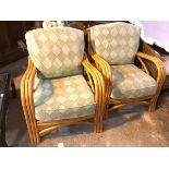 A pair of cane chairs with hoop backs and arms, with green geometric upholstery seat cushions,