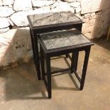 A pair of ebonised Chinese nesting tables, each with a deep relief carved top depicting Soldiers
