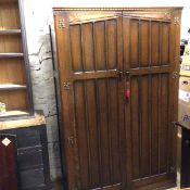 An oak wardrobe with dentil cornice above a pair of inset panel doors, enclosing a plain interior,