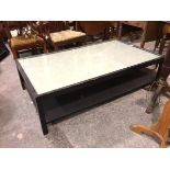 An ebonised two tier rectangular coffee table with inset glass top, on square supports (41cm x 153cm