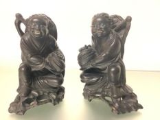 A pair of Chinese carved ebonised or rosewood figures of laughing children, each modelled holding