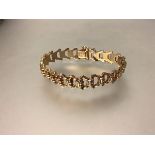 A yellow metal fancy link bracelet, stamped 21k, of shaped links spaced by reeded bars, further